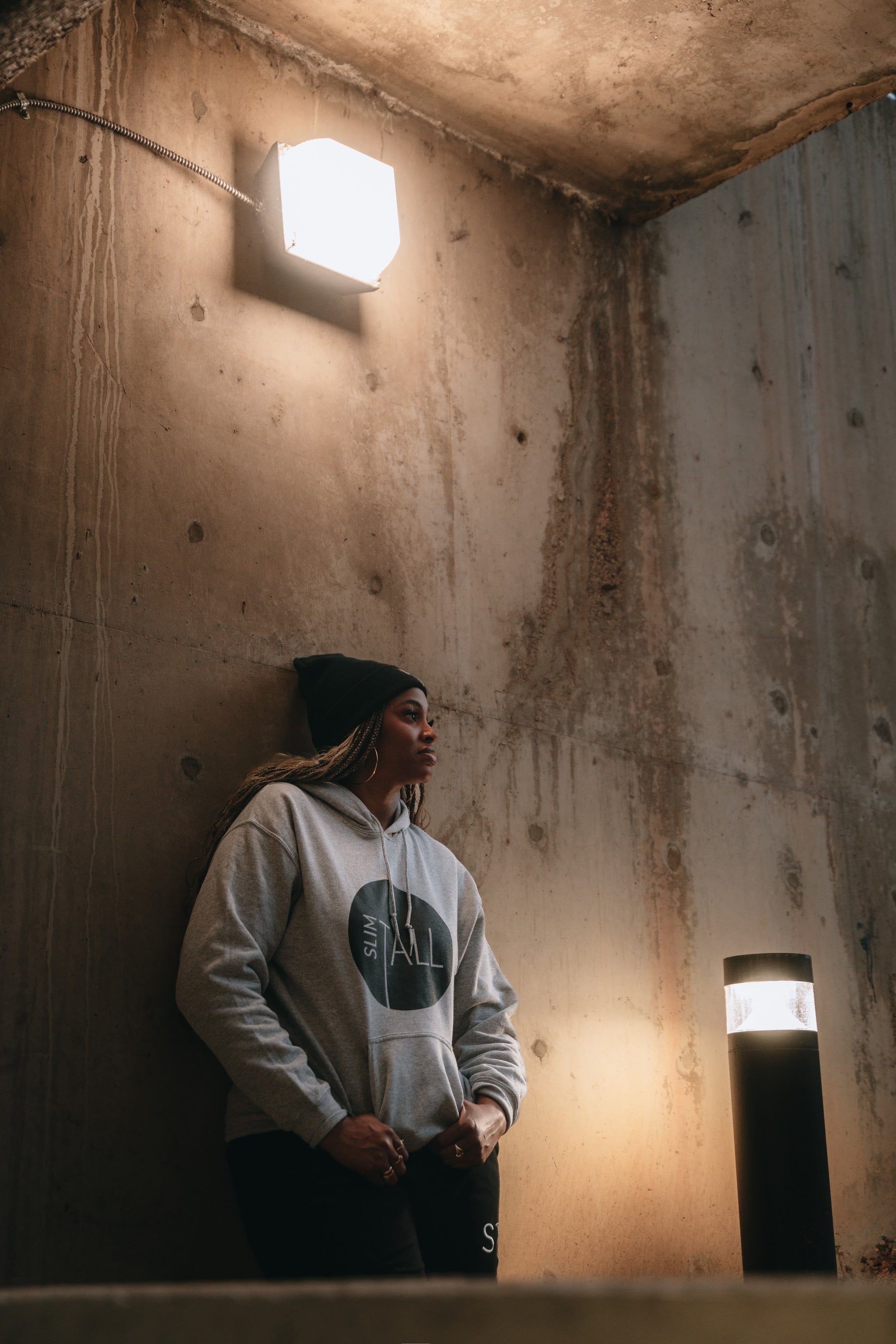 SlimTall black beanie and grey circle-logo hoodie, full-length shot by a lamp